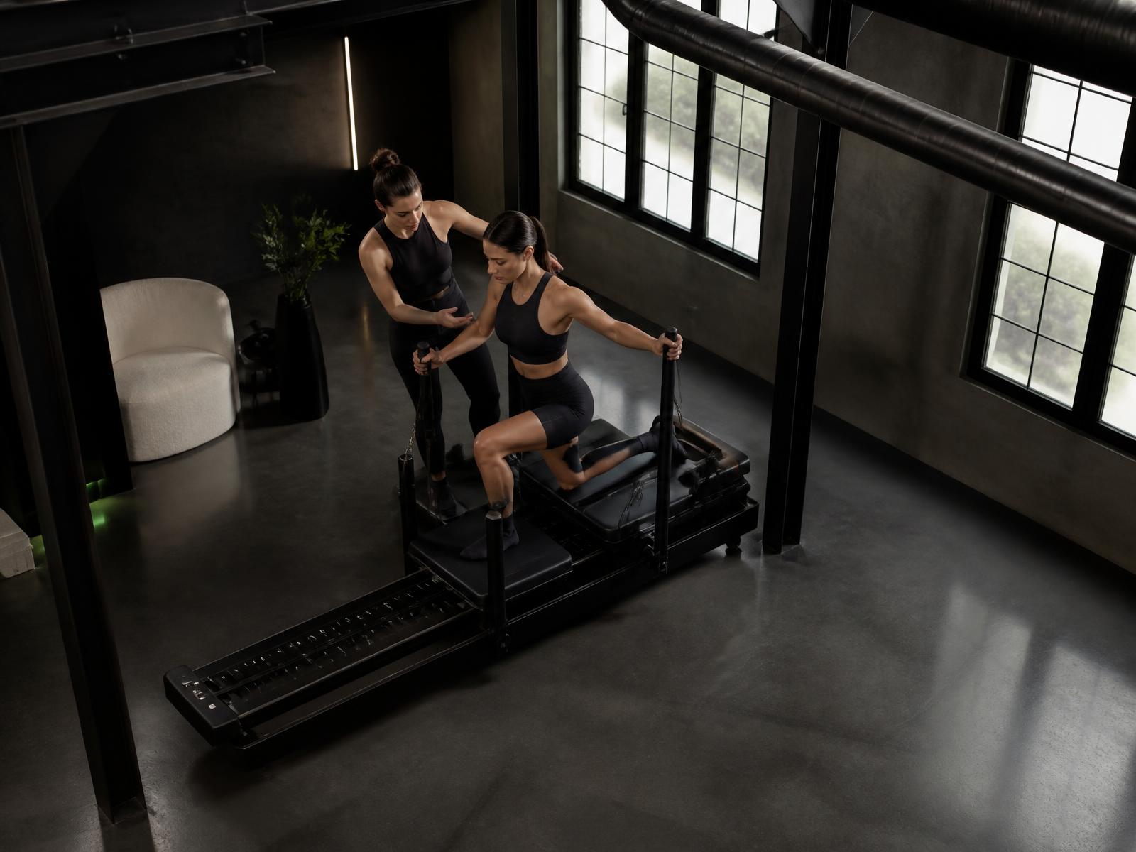 Instructor coaching a client 1 on 1 on a Lagree Mini Pro in a dark boutique studio.